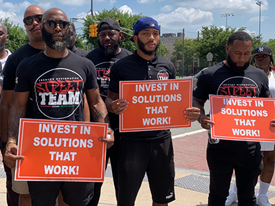 Newark Community Street Team holding signs that read 'Invest in Solutions that Work'